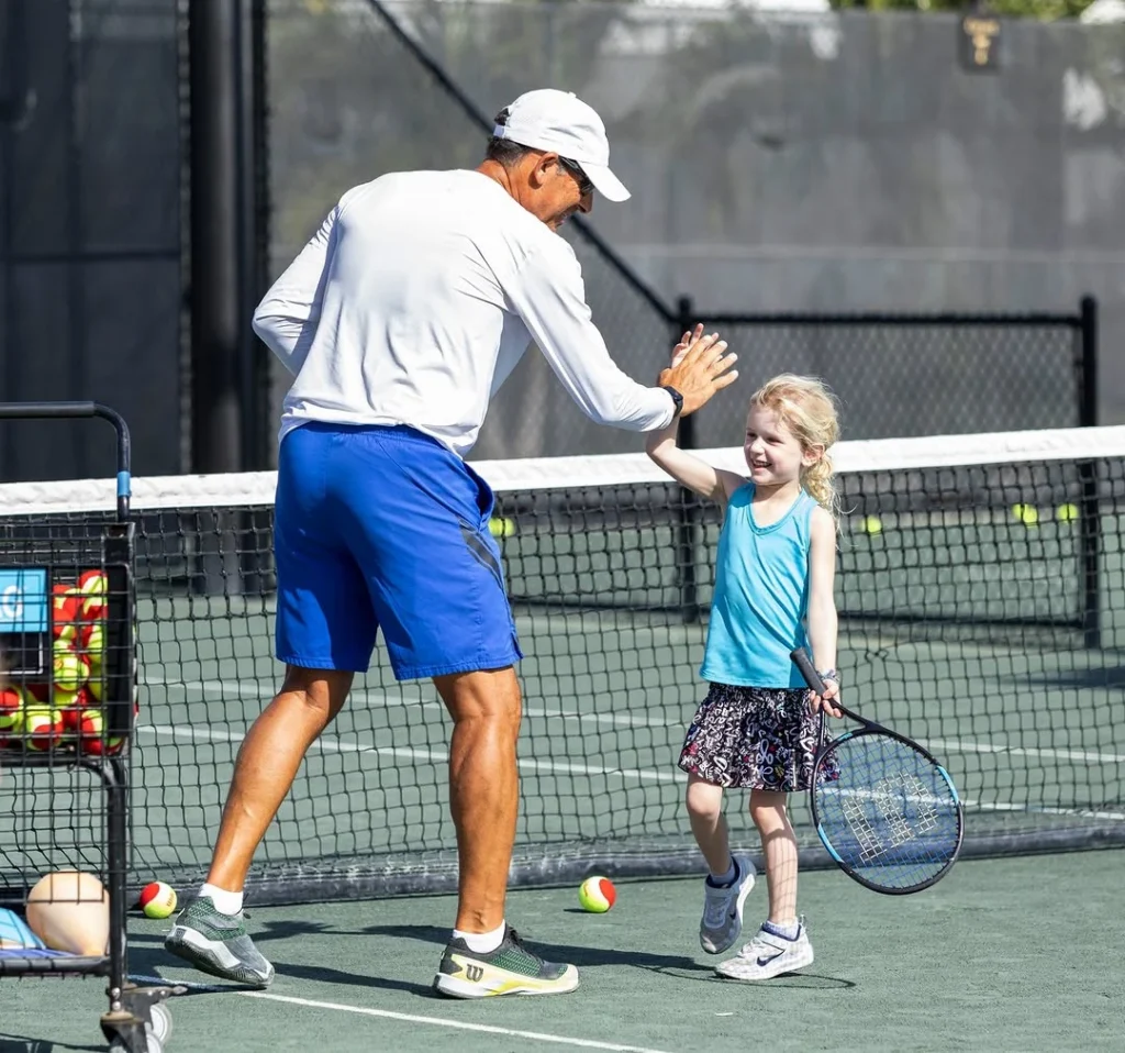 Tennis instructor high-fiving a young player during a junior tennis lesson at Mirasol in Palm Beach Gardens