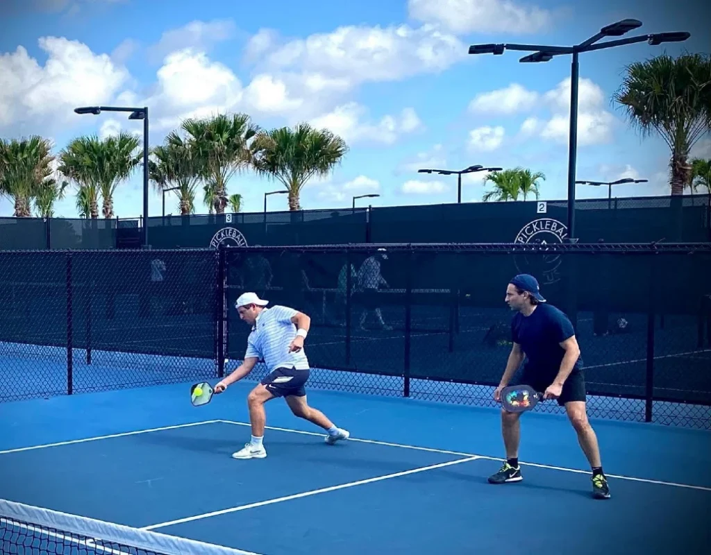 Two players competing in doubles on Lotus Boca Raton blue pickleball courts
