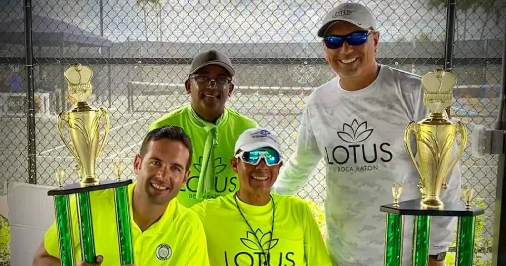 Four Lotus Boca Raton players holding tournament trophies in community branded apparel