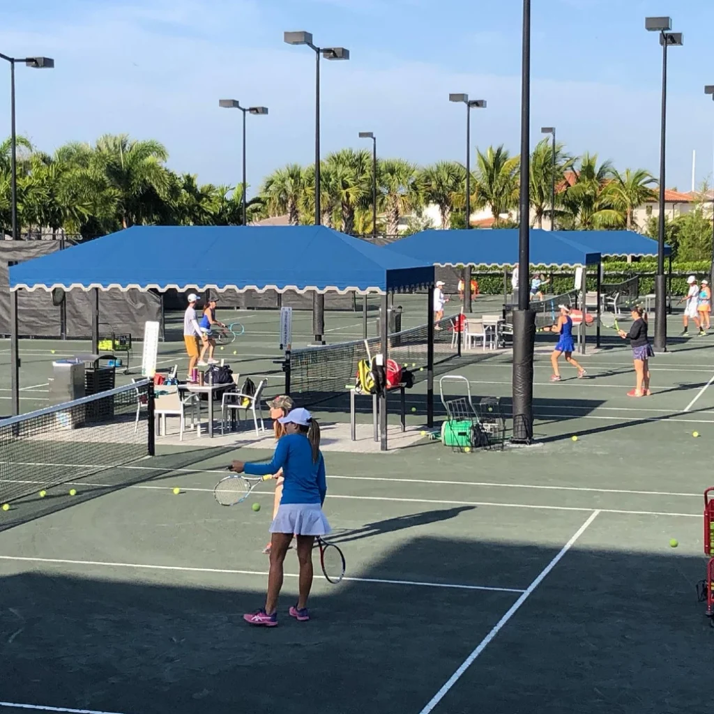 Active tennis clinic with multiple players on Har-Tru courts and shade canopies at Seven Bridges